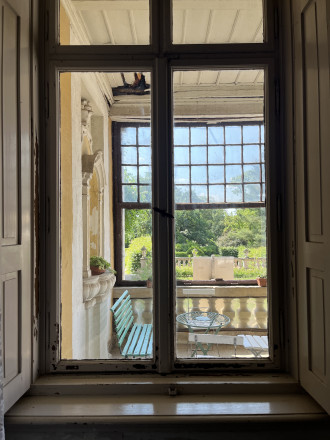 Blick durch geschlossenes Fenster des Innenraumes auf Terrasse und Schlosspark im Hintergrund